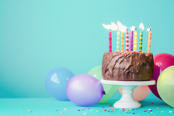 Шоколадний торт на день народження з різнокольоровими свічками та повітряними кульками
 - Фото, зображення