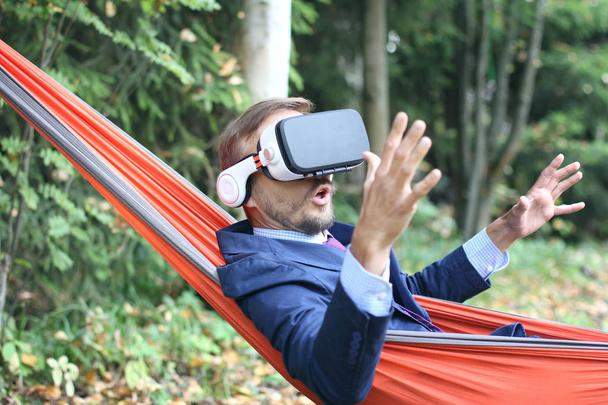 Surprised businessman uses vr glasses, resting in a hammock on nature. Virtual reality or future technology concept.  - Foto, Imagem