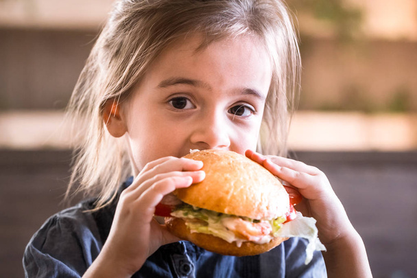 Ładna dziewczynka jedzenie Kanapki w kawiarni, pojęcie posiłek fast food dla dzieci - Zdjęcie, obraz