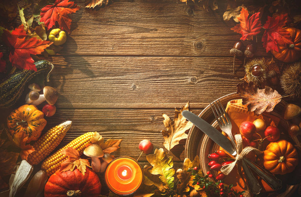 Autumn background from fallen leaves, fruits with vintage place setting and burning candle on old wooden table. Thanksgiving day concept - Photo, image