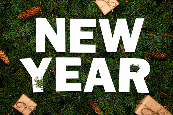 Mots Nouvel An sur les branches de sapin vert avec de petites boîtes-cadeaux. Concept de nature créative. Composition minimale des vacances. Couché plat
 - Photo, image