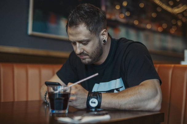 Young attractive man looking at mobile phone screen and drinking soda. - Valokuva, kuva