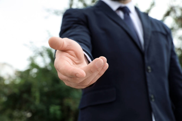 Businessman giving helping hand on blurred background outdoors - Photo, image