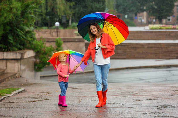 Happy mother and daughter with bright umbrella under rain outdoors - Foto, Imagen