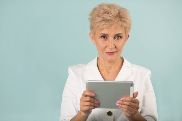 stylish elderly woman with short hair in a white jacket with a tablet in her hands - Foto, Imagem