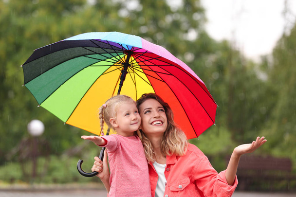 Happy mother and daughter with bright umbrella under rain outdoors - Фото, изображение