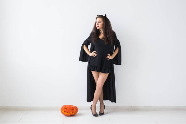 Femme gothique mignon dans des vêtements de style halloween avec citrouille dans les mains sur fond clair avec espace de copie
 - Photo, image
