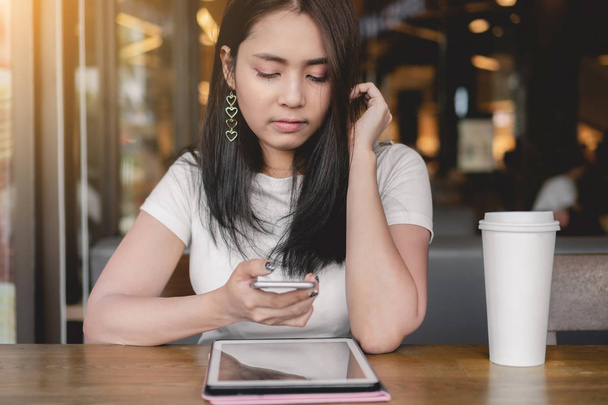  женщина с помощью смартфона с пустым экраном, сидя за деревянным столом с цифровым планшетным ПК и чашкой белого кофе в кафе
 - Фото, изображение