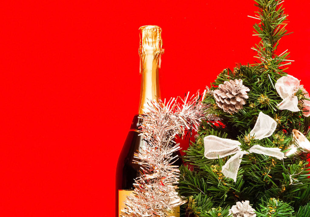 Блискучий різдвяний та новорічний декор. Декоративна ялинка зі срібною прикрасою та пляшка шампанського, прикрашена святковою тематикою на червоному тлі, крупним планом, місце для тексту
 - Фото, зображення