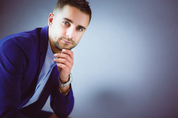 Young businessman sitting isolated on grey background - 写真・画像