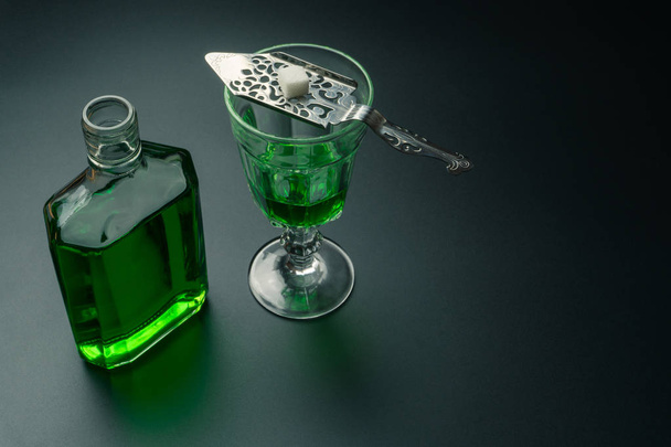 an absinthe bottle, a glass of absinthe and a stainless steel slotted spoon with the sugar cube on the table - Photo, image