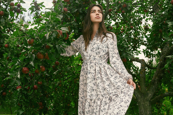 Porträt einer hinreißenden brünetten Frau im klassischen Kleid, die zwischen Apfelbäumen posiert - Foto, Bild