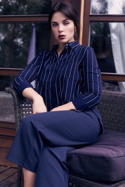 Portrait of gorgeous brunette woman in fashion classic woolen suit posing in chair on a stylish terrace - Foto, Imagen