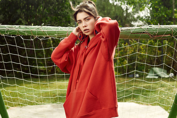 Портрет чудової брюнетки в моді червоний светр позує на спортивному полі
 - Фото, зображення