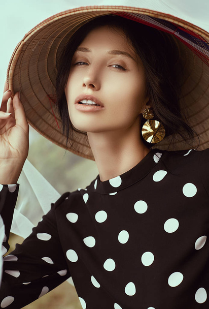 Portrait of a gorgeous bright brunette woman in fashion dress with straw chinese hat posing in garden - Photo, Image