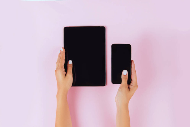 Women hands holding tablet computer and smartphone on pink background. - Fotoğraf, Görsel