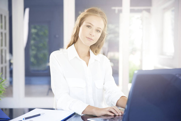 Beautiful young businesswoman using her laptop and working while sitting at office desk. - Foto, Bild