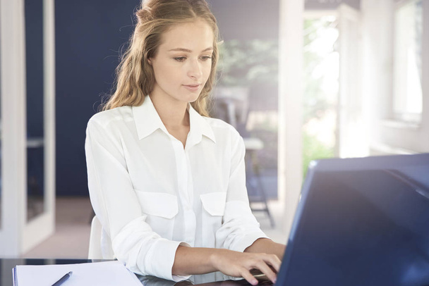Confident young businesswoman using her laptop while sitting at office desk and working, - Foto, immagini
