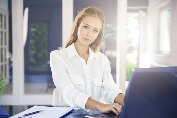 Beautiful young businesswoman using her laptop and working while sitting at office desk. - Foto, imagen