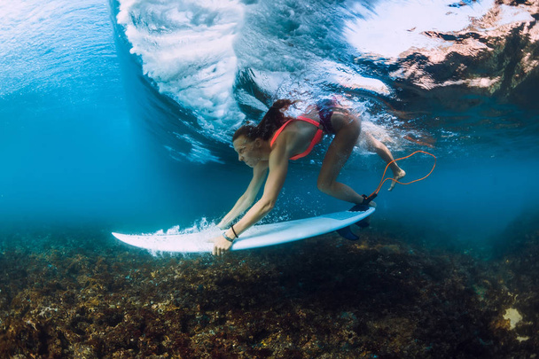 Professionele surfer vrouw met surfplank duik onderwater met ocean wave. - Foto, afbeelding