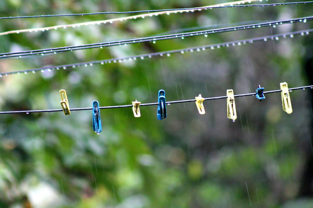 Clothes hooks on wires for drying clothes. Rainy autumn weather. Wires for hanging lingerie with drops of water. The yellow and blue clothes hooks hang on them. - Photo, Image