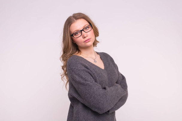 Emotions et concept de personnes - Jeune femme sur fond blanc dans un pull tricot gris se serrant dans ses bras en regardant la caméra
 - Photo, image