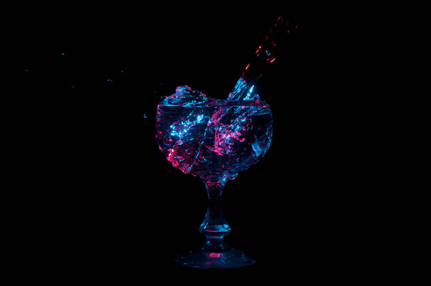 Agua desbordante en la taza bajo luces de colores sobre un fondo negro
 - Foto, Imagen