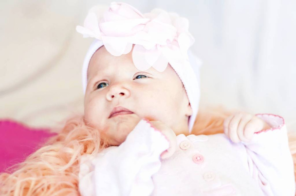 Una graziosa neonata caucasica con una fascia di fiori sdraiata su un letto. Uno sguardo curioso. Un nuovo concetto di vita. Un bambino di un mese
. - Foto, immagini