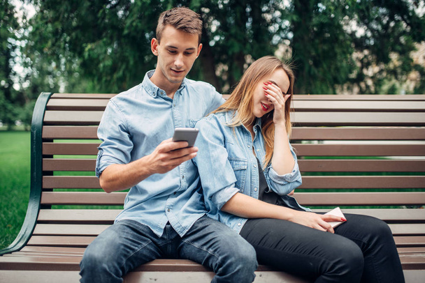 携帯電話の常習している人、公園のベンチにカップルします。男と女の中毒、彼らのスマート フォンを使用して - 写真・画像