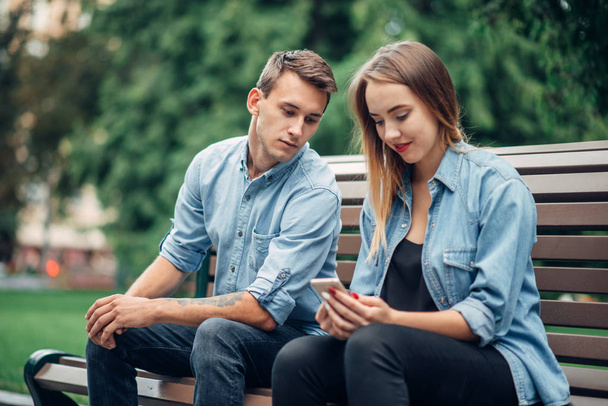 Phone addiction, young couple on the bench in park. Man and woman using their smartphones, addicted people - Фото, зображення