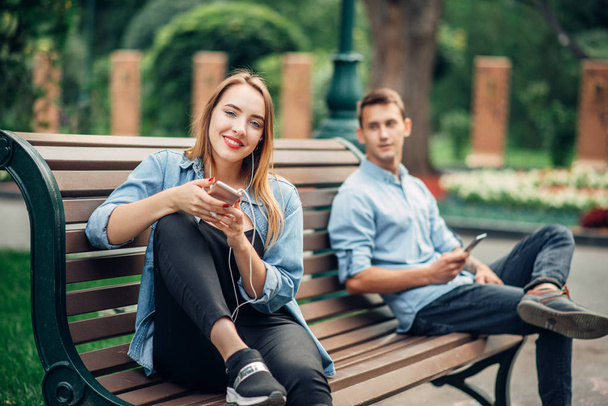 Phone addiction, couple ignoring each other on the bench in park. Man and woman using their smartphones, social addicted people - Фото, зображення