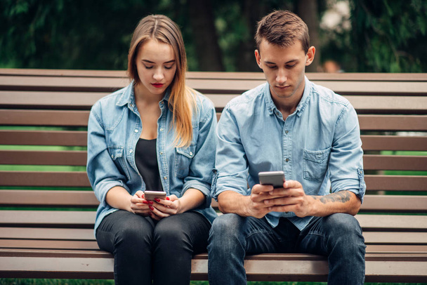 Dépendance téléphonique, couple de toxicomanes utilisant des smartphones sur le banc dans le parc, personnes dépendantes sociales
 - Photo, image