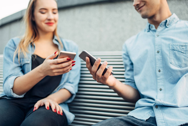 Handysucht, süchtiges Paar, das auf der Bank sitzt und auf Smartphones schaut, sozialsüchtige Menschen - Foto, Bild