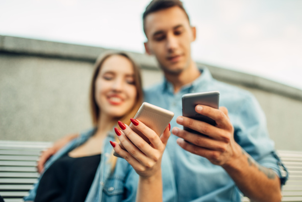 Τηλέφωνο εθισμό, πορτρέτο του εξαρτημένος ζευγάρι χρησιμοποιώντας smartphones στον πάγκο στο πάρκο, κοινωνική εθισμένος άτομα - Φωτογραφία, εικόνα