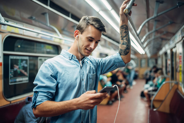 Young man using phone in metro, addiction problem, social addicted people, modern underground lifestyle - Фото, изображение