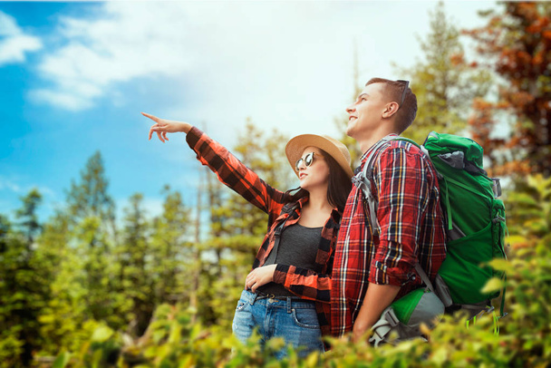 Couple of tourists with backpacks traveling through the woods. Hiking in summer forest. Hike adventure of young man and woman - Foto, afbeelding