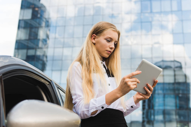 Meisje met de Tablet PC in de buurt van auto voor wolkenkrabber - Foto, afbeelding