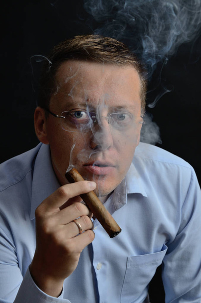 Male model, 35 years old. Man with glasses, wearing light blue shirt, holding cigar in his hand. - Fotoğraf, Görsel