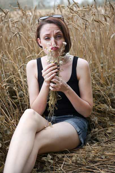 mladá dívka s kyticí sedí poblíž pšeničné pole. Si vybírá z okvětních lístků a zajímá Vás, k milovat nebo nemilovat, staré lidové legendy a tradice. - Fotografie, Obrázek