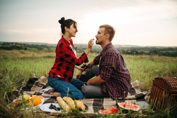 Woman feeds grapes to her man on picnic in summer field. Romantic junket of man and woman, love couple happy together - Foto, imagen