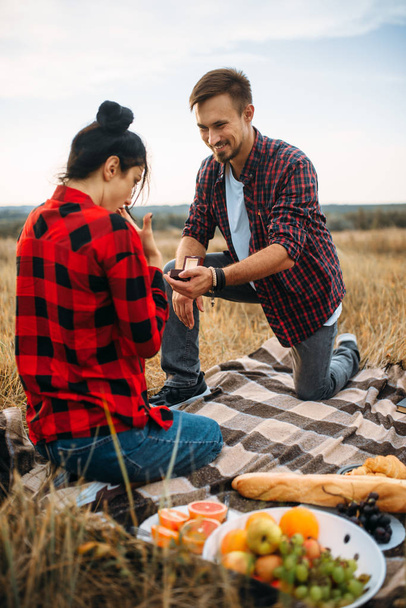 Man maakt een huwelijksaanzoek op romantische picknick in zomer veld. Kwark van man en vrouw, gelukkige momenten - Foto, afbeelding