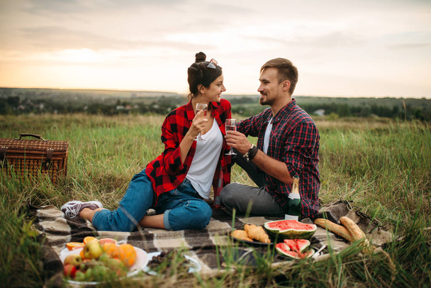 Love couple drinks wine, picnic in summer field. Romantic junket, man and woman leisure together, happy family weekend - Foto, immagini