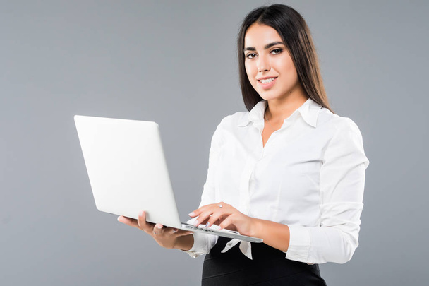 Jovem mulher sorridente feliz segurando laptop e enviando e-mail isolado em fundo cinza
 - Foto, Imagem