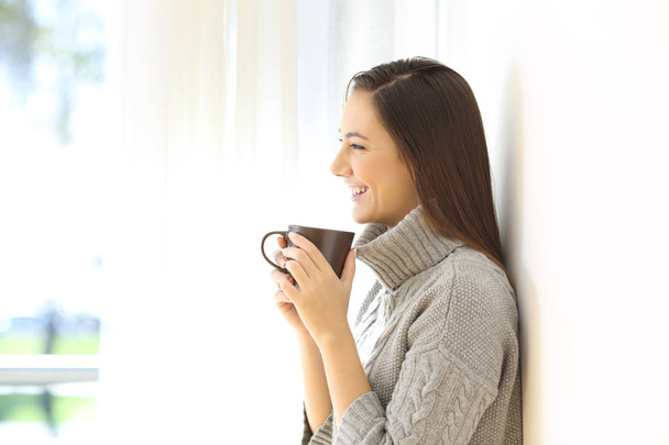Profile of a woman holding a coffee mug standing at home in winter - Fotoğraf, Görsel