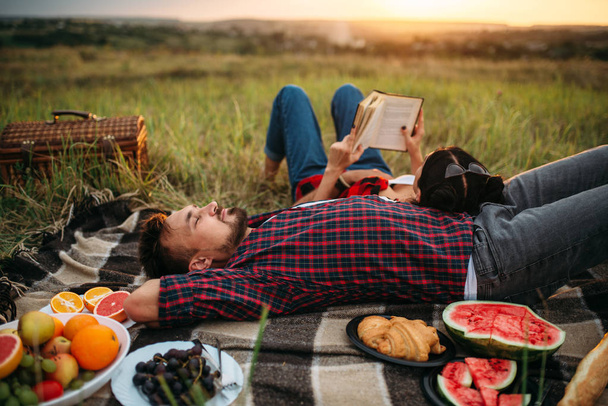 Love couple resting together, picnic in the field. Romantic junket on sunset, man and woman on outdoor dinner, happy family - Photo, Image