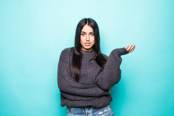 Portrait of a lovely young woman in sweater with open palm isolated over blue background - Φωτογραφία, εικόνα