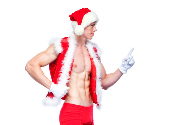 Sexy Santa Claus pointing in white blank sign. Young muscular man wearing Santa Claus hat demonstrate his muscles. Isolated on white background. - Photo, Image