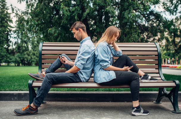 Phone addicted people, couple on the bench. Man and woman using their smartphones in summer park, addiction - Foto, Bild
