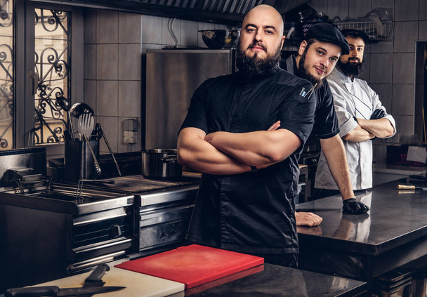 Команда профессиональных бородатых поваров, одетых в униформу, стоящих на кухне
. - Фото, изображение
