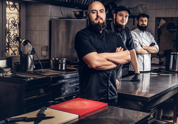 Team of professional bearded cooks dressed in uniforms standing in kitchen. - Photo, Image